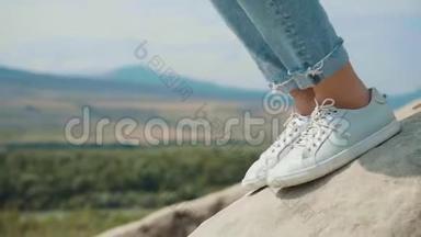 孤独的<strong>人与自然</strong>，拍摄近腿的女孩穿着白色运动鞋和短牛仔裤，女士坐在岩石上。